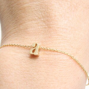 May include: A gold chain bracelet with a small, cursive letter 'a' charm.