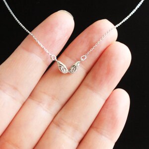 May include: A silver chain necklace with a delicate pair of angel wings pendant.