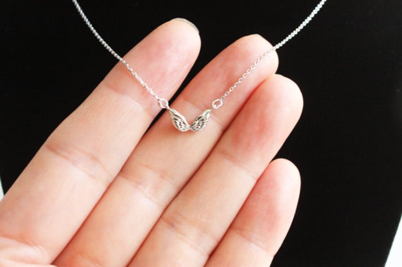 May include: A silver chain necklace with a delicate pair of angel wings pendant.