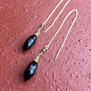 May include: A pair of black onyx gemstone dangle earrings with gold chain and wire accents. The earrings are approximately 2 inches long.