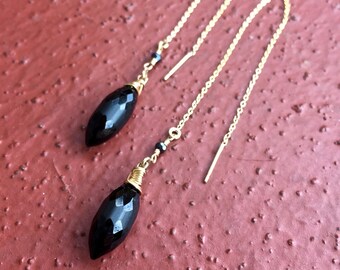 May include: A pair of black onyx gemstone dangle earrings with gold chain and wire accents. The earrings are approximately 2 inches long.