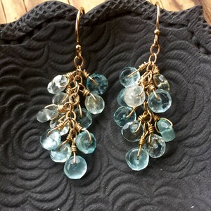 May include: Gold dangle earrings with a cluster of light blue aquamarine gemstones.