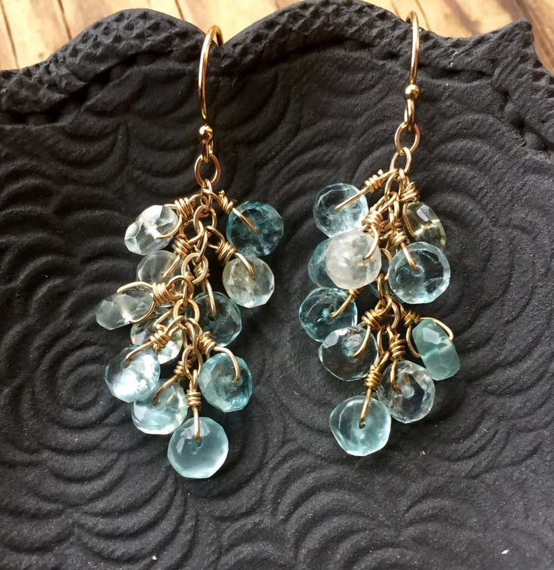 May include: Gold dangle earrings with a cluster of light blue aquamarine gemstones.