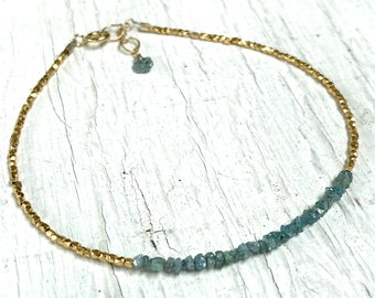 May include: A gold chain bracelet with a row of light blue rough diamonds. The bracelet has a gold clasp.