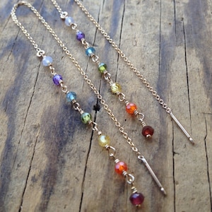 Puede incluir: Tres cadenas de oro con cuentas de piedras preciosas de colores. Las cadenas están superpuestas y presentan cuentas de diferentes colores, incluyendo morado, azul, verde, amarillo, naranja y rojo.