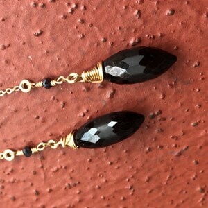 May include: A pair of long black gemstone earrings with gold wire wrapping and a gold chain. The earrings have a black bead on each chain.