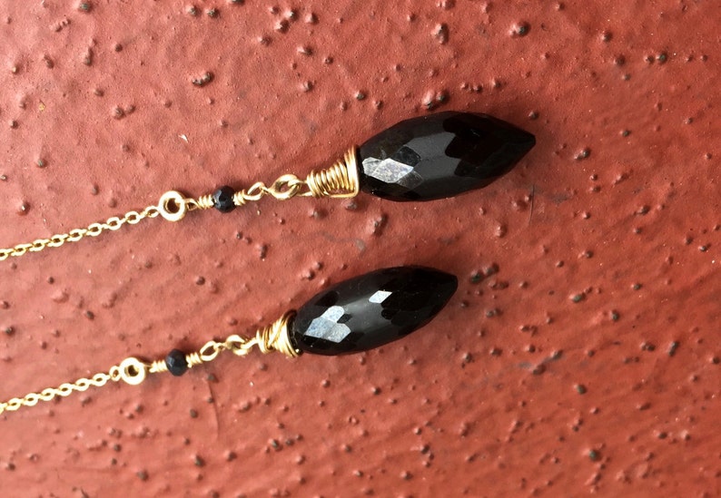 May include: A pair of long black gemstone earrings with gold wire wrapping and a gold chain. The earrings have a black bead on each chain.