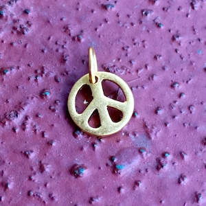 May include: A gold-colored peace sign charm pendant. The charm is a simple, classic design with a circular shape and a peace symbol in the center.