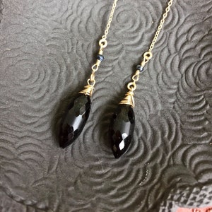 May include: A pair of long, dangling earrings with black faceted gemstone drops and gold chain accents.