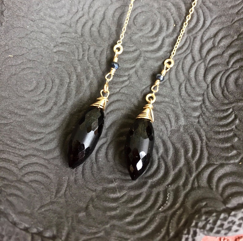 May include: A pair of long, dangling earrings with black faceted gemstone drops and gold chain accents.