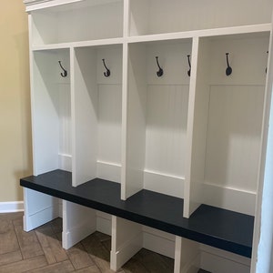 May include: White wooden entryway bench with a black top and four hooks. The bench has three cubbies with a shelf above each cubby.