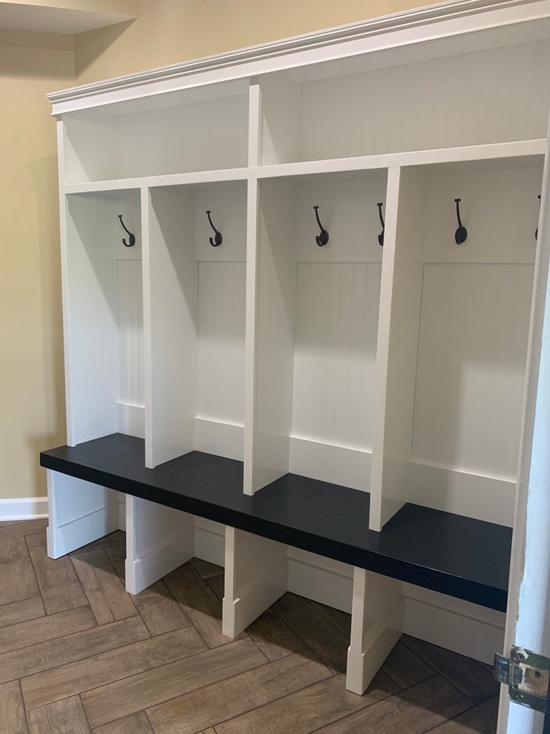 May include: White wooden entryway bench with a black top and four hooks. The bench has three cubbies with a shelf above each cubby.