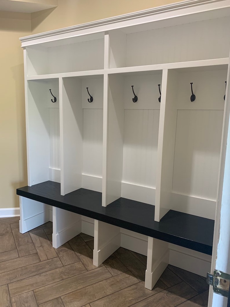 May include: White wooden entryway bench with a black top and four hooks. The bench has three cubbies with white shelves.