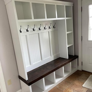 May include: White wooden entryway bench with a dark brown wood top, open cubbies, and hooks for hanging coats and bags.