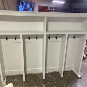 May include: White wooden coat rack with four sections, each with a shelf and hooks. The rack has a simple design and is ideal for a hallway or entryway.