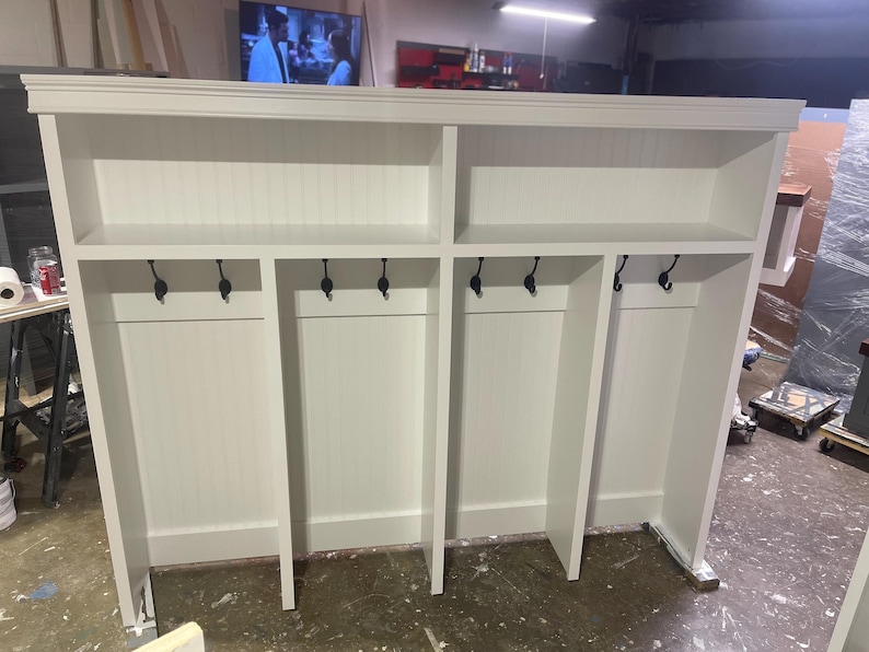 May include: White wooden coat rack with four sections, each with a shelf and hooks. The rack has a simple design and is ideal for a hallway or entryway.