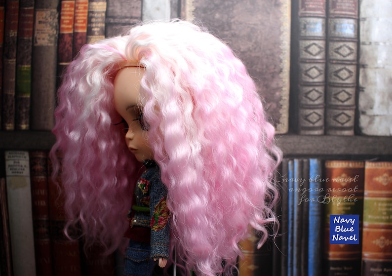 May include: A doll with long, curly pink and white hair. The doll is wearing a denim jacket and jeans. The doll is standing in front of a bookcase.