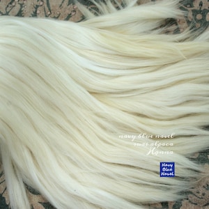 May include: A close-up of a bundle of white alpaca fibre. The fibre is soft and fluffy, and it is perfect for spinning or felting. The text "navy blue navel super alpaca llama" is visible in the image.