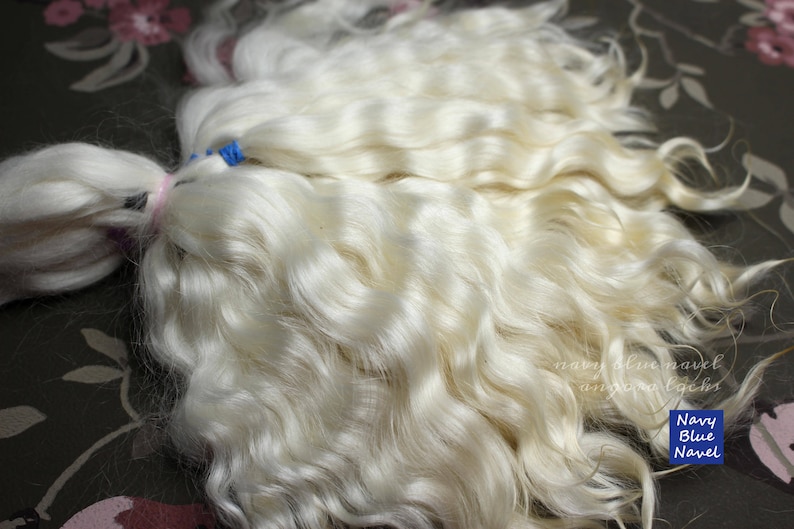 May include: A large bundle of white, wavy human hair extensions. The hair is tied together with a pink ribbon and blue rubber bands.