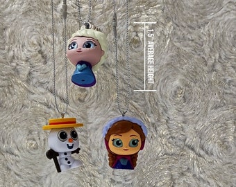 Può includere: Tre ciondoli dei personaggi del film Frozen, ciascuno sospeso da una catena d'argento. I ciondoli sono alti circa 3,8 cm. I personaggi includono Elsa, Anna e Olaf, ognuno con tratti somatici e abiti distintivi.