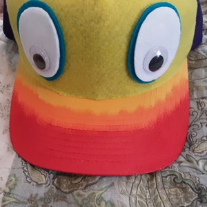 May include: A yellow felt hat with orange and red trim. The hat has two large white eyes with black pupils.