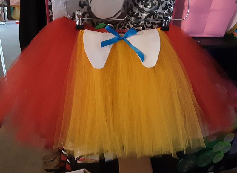May include: A red and yellow tulle tutu with a white felt collar and a blue ribbon bow.