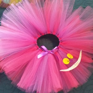 May include: A pink and purple tulle tutu with a white felt Cheshire Cat grin and yellow felt eyes.