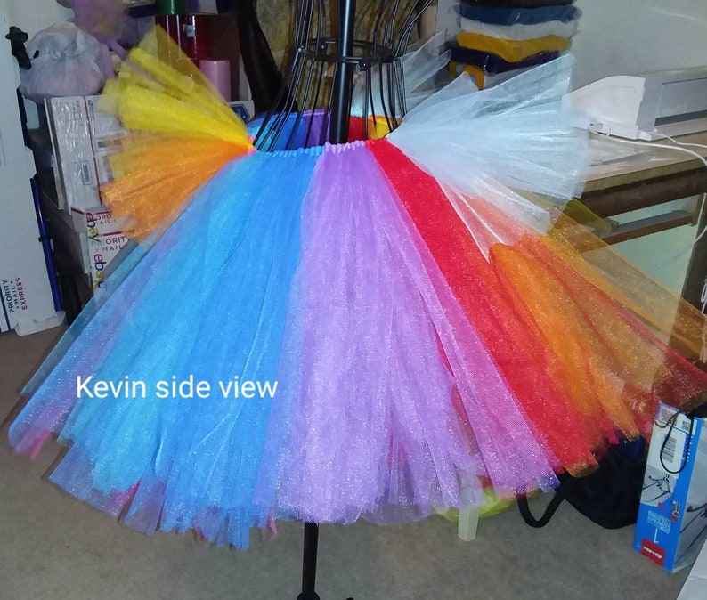 May include: A rainbow tulle tutu skirt with a white tulle overlay. The skirt is on a mannequin and the text "Kevin side view" is visible in the image.