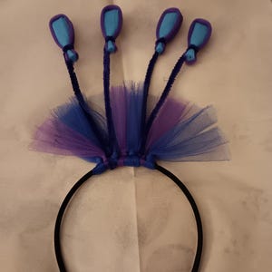 May include: A black headband with a purple and blue tulle bow and five blue felt balloons attached to pipe cleaner stems.