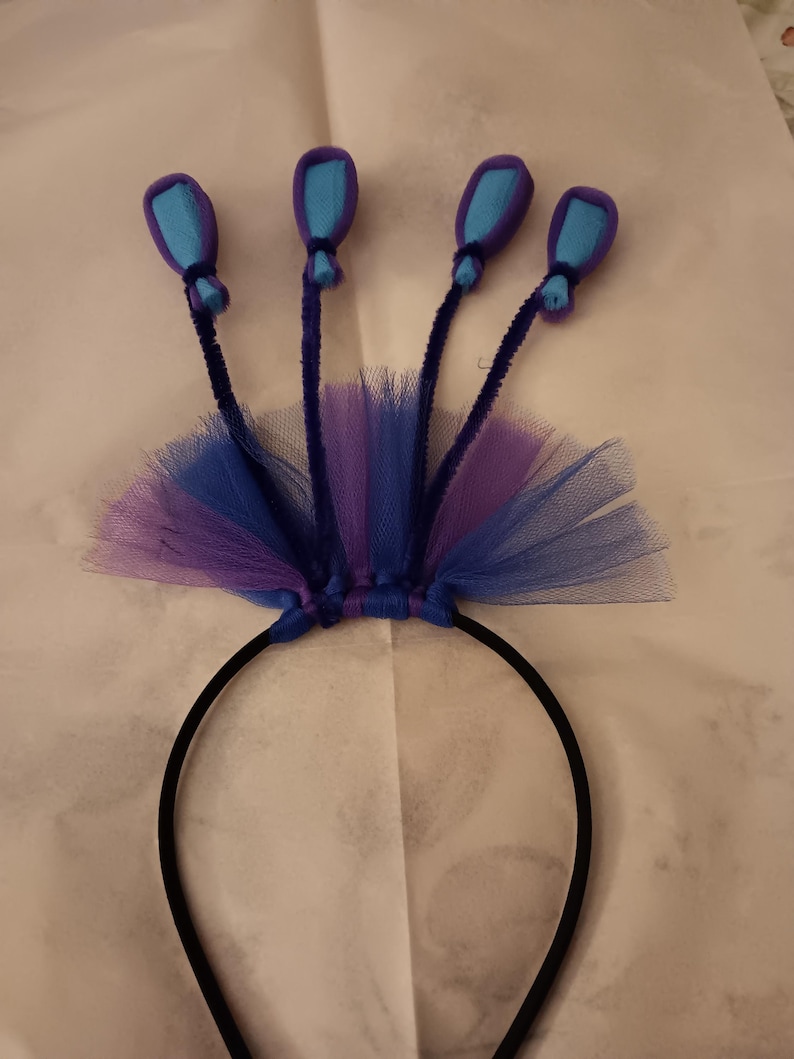 May include: A black headband with a purple and blue tulle bow and five blue felt balloons attached to pipe cleaner stems.