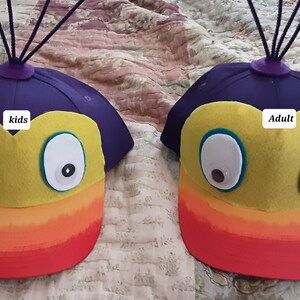 May include: Two felt hats with rainbow brims and googly eyes. One hat says "kids" and the other says "adult".