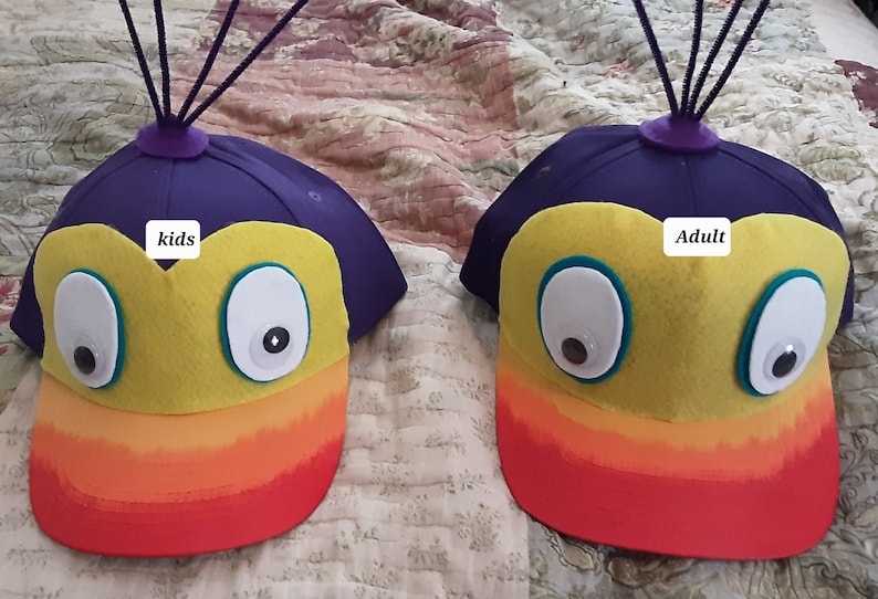 May include: Two felt hats with rainbow brims and googly eyes. One hat says "kids" and the other says "adult".