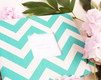 May include: A turquoise and white chevron patterned scrapbook with a white window cut out. The window has a white card inside with the text "The modern way to store your love treasures".