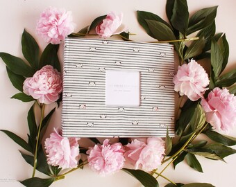 May include: A white photo album with black stripes and a panda bear pattern. The album has a white window for a photo. The album is surrounded by pink peonies and green leaves.