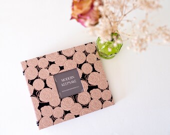 May include: A black and rose gold photo album with a rose pattern and the text "MODERN KEEPSAKE" on the front.