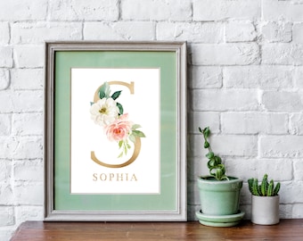 May include: A framed print with a gold letter S decorated with watercolor flowers in shades of pink and white. The name "Sophia" is printed below the letter.