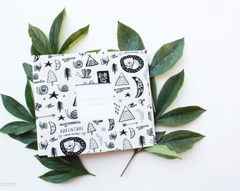 May include: A white baby book with a black and white illustration of a forest scene. The book has a window on the front cover with the text "The Modern Baby Book" printed below it.