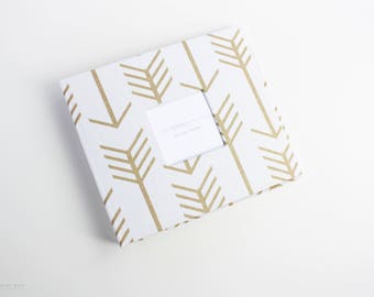 May include: White photo album with a gold arrow pattern and a rectangular window for a photo. The window has the text "Remember All The Little Moments" inside.