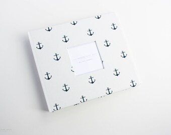 May include: White photo album with a navy blue anchor pattern. The album has a blank white insert page for photos.