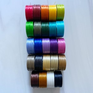 Peut inclure: Une collection de 20 bobines de fil de diff&eacute;rentes couleurs, dont le rouge, le vert, le bleu, le violet, l'orange, le jaune, le marron et le noir. Les bobines sont dispos&eacute;es en pile, la bobine du haut &eacute;tant rouge et la bobine du bas &eacute;tant noire.