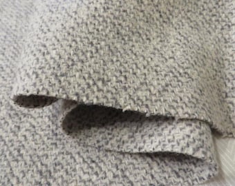 May include: Close-up of a textured fabric in shades of gray and white. The material has a woven pattern with a slightly rough, tactile appearance. The fabric is folded over, revealing the edges and layers of the material. Ideal for apparel or home decor.