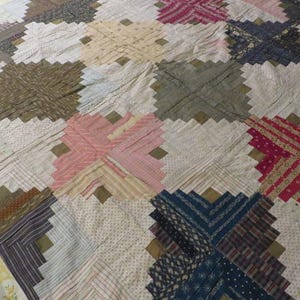 May include: A patchwork quilt featuring a log cabin block pattern composed of various fabric strips in shades of pink, blue, brown, white, and grey. The quilt is bordered by a light yellow fabric with a subtle floral print pattern throughout.