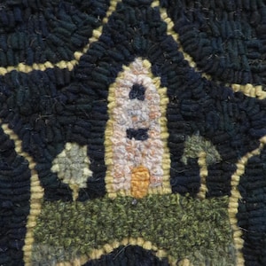 May include: A close-up of a hand-stitched rug with a star-shaped design. The star features a white building with a yellow door and two black windows. The background is a dark blue color.