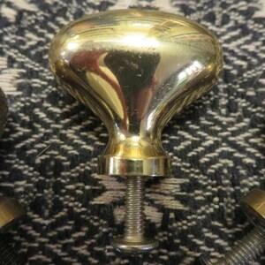 May include: A polished brass cabinet knob with an oval-shaped head and a smooth, reflective surface. The knob features a central threaded metal bolt extending from the base, designed for attachment to furniture or cabinetry doors.