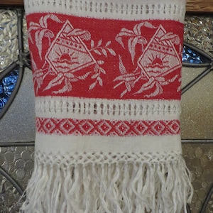 May include: White kitchen towel with red and white embroidered design. The towel has a fringe border and a woven pattern.