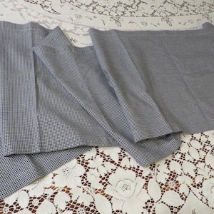May include: Several pieces of blue and white checkered fabric are arranged on a white lace tablecloth. The fabric is folded and appears to be a medium weight, suitable for clothing or home decor projects.