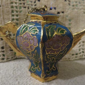 May include: A small blue and gold teapot with floral designs. The teapot has a lid and a spout. The teapot is made of metal and has a shiny finish.