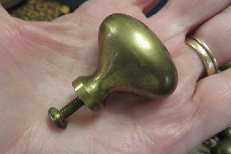 May include: A brass cabinet knob with a smooth, rounded, teardrop-shaped head and a tapered neck. The knob features a threaded metal screw extending from the base, designed for attachment to furniture or cabinetry doors and drawers.