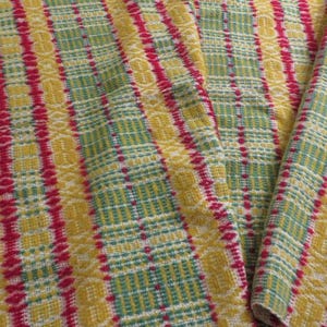 May include: A woven textile fabric featuring a repeating vertical striped pattern in vibrant shades of mustard yellow, bright magenta, and soft sage green. The material displays a complex interlaced texture with small geometric motifs throughout.