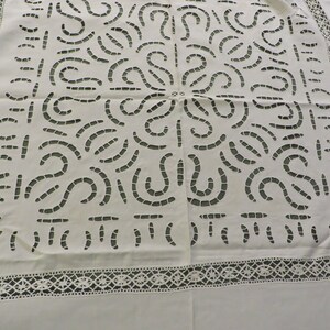 May include: White linen tablecloth with a delicate lace border and a central design of intricate cut-out patterns.